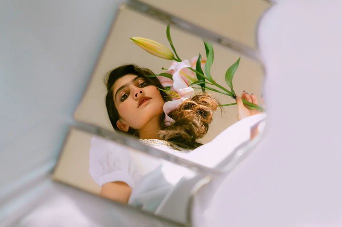 A photograph of a woman holding pink lilies, viewed as a reflection in a small mirror.
