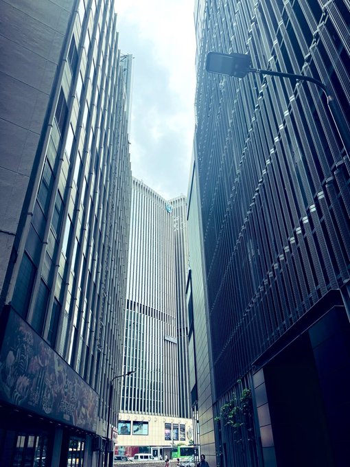 A low-angle view looking up at towering modern skyscrapers framing a narrow strip of cloudy sky, with a street lamp extending into view.