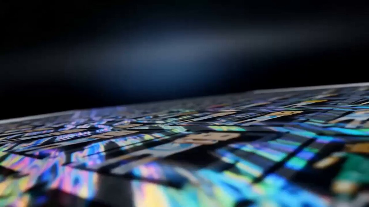 The image shows a close-up view of a black surface with a colorful, abstract design that appears to be made up of many small rectangles or squares. The background is dark, which contrasts with the vibrant colors of the design on the surface. The text in the image reads "Today we announced our new physical trading cards in partnership w/ OpenSea and Apechain". This suggests that there might be a connection between the colorful abstract design and the trading card game or event happening today.