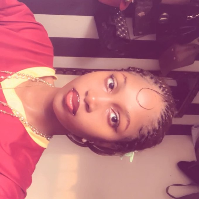 A sideways, purple-tinted selfie of a woman with braided hair, a large hoop earring, and layered necklaces posing indoors.