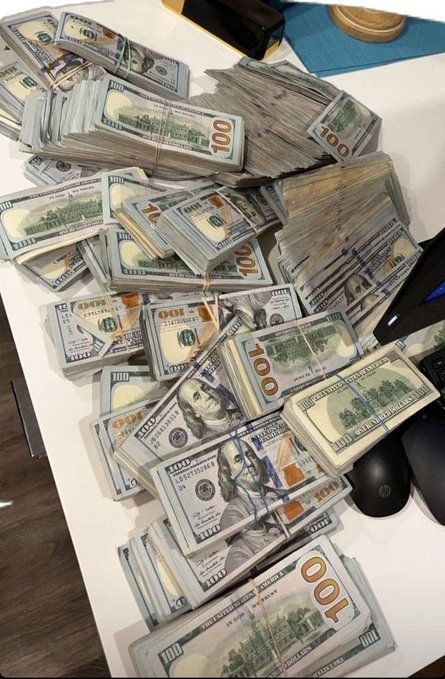 Stacks and bundles of $100 US bills arranged on a table next to a computer mouse and other items.