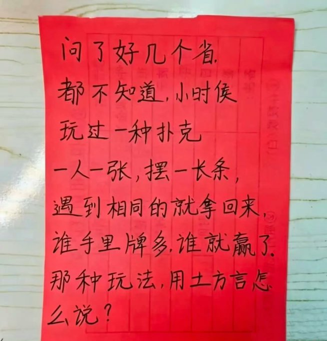A handwritten note on red paper in Chinese characters asking about a children's card game they played as kids in several provinces, where players laid out cards in a row and competed to collect matches, asking what it's called in the local dialect.