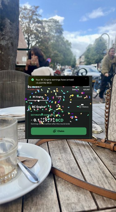 A mobile screenshot of a 'BC Engine' crypto rewards app claiming a 0.144575 BCD earnings balance, overlaid on a photo of an outdoor café table.
