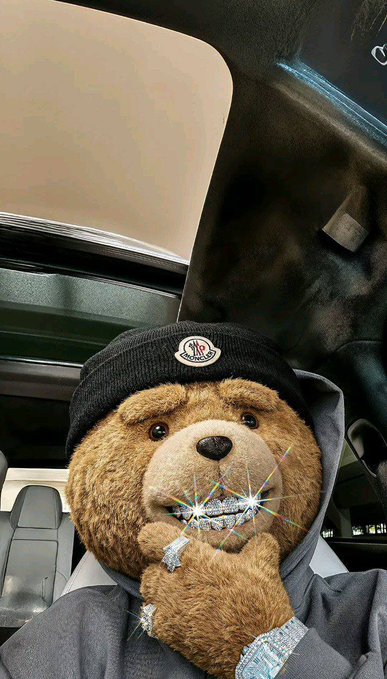 A brown teddy bear wearing a Moncler beanie sits inside a car, holding a "blinged-out" piece shaped like its paw—styled as a diamond-studded ice accessory—dressed in a Moncler hoodie. The post's caption ("market is green and I lob greens") ties in with the image through a diamond/crypto slang joke, where the bear's "iced" paw symbolizes the "greens" (profits) being celebrated on a green market day.