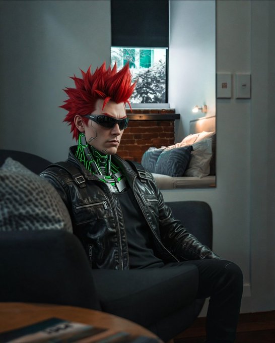 A cosplay portrait of the character Caesar from the anime Cyberpunk: Edgerunners, featuring spiky red hair, dark sunglasses, a glowing green neck implant, and a black leather jacket while sitting on a couch.