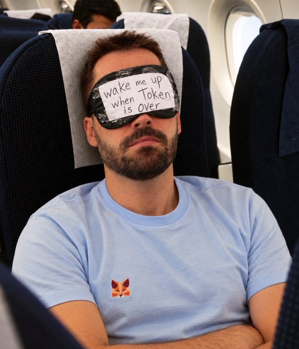 A bearded man sleeps on a plane wearing a "Wake me up when Token is Over" eye mask and a light blue shirt with a fox logo, humorously capturing the exhaustion from Day 1 of Token2049 mentioned in the post.