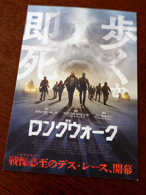 A Japanese promotional flyer for the movie 'ロングウォーク' (The Long Walk), featuring characters walking down a road with a wolf image, starring Stephen King and Francis Lawrence.