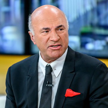 Kevin O'Leary, known from Shark Tank, appears in a TV interview setting wearing a dark suit with a red pocket square, speaking about the U.S. government's reported multi-trillion dollar Bitcoin acquisition plans.
