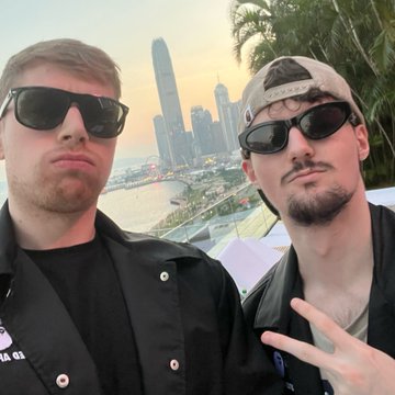 Two men wearing sunglasses pose for a selfie with a modern city skyline and waterfront visible in the background, with one making a peace sign, capturing the travel and lifestyle experiences referenced in the caption about opportunities in the crypto industry.