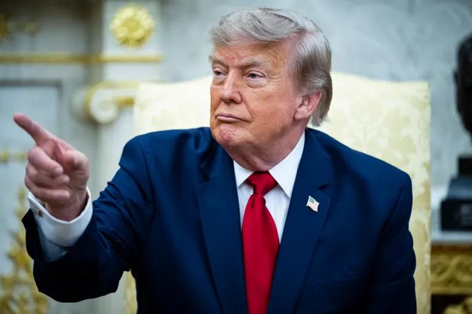 Donald Trump, in a suit and red tie with an American flag pin, points with his left hand. The image is used to visually suggest a connection between Trump speaking and the XRP financial reset mentioned in the post.