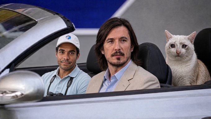 A man in a tan blazer and a man wearing a "VB" cap drive a convertible alongside a white cat, parodying the famous "Mean Girls" scene to humorously suggest they are "replacing the entire financial system."