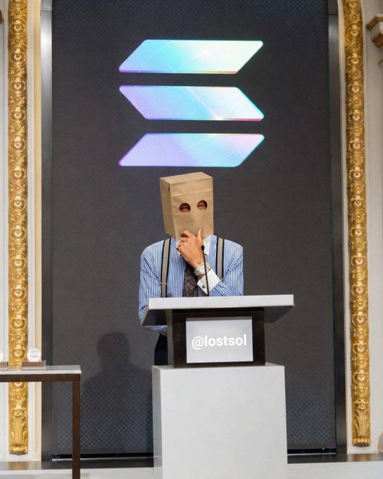 A person wearing a paper bag over their head stands at a podium marked '@iostsol' beneath a glowing Solana logo, with their hand on their chin in a thoughtful pose.