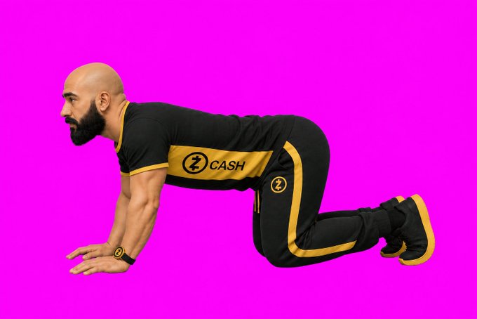 A bald man with a beard wearing black and gold 'Z CASH' branded athletic wear, posed in a crawling position against a bright pink background.
