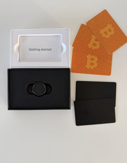 A product layout shows a small black device in its packaging box with a card reading 'Getting started', alongside three orange 'B' branded cards and two black metal plates.
