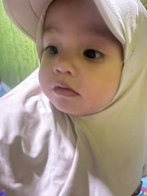 A close-up photo shows a baby wearing a cream-colored hooded garment, looking off to the side with large dark eyes.
