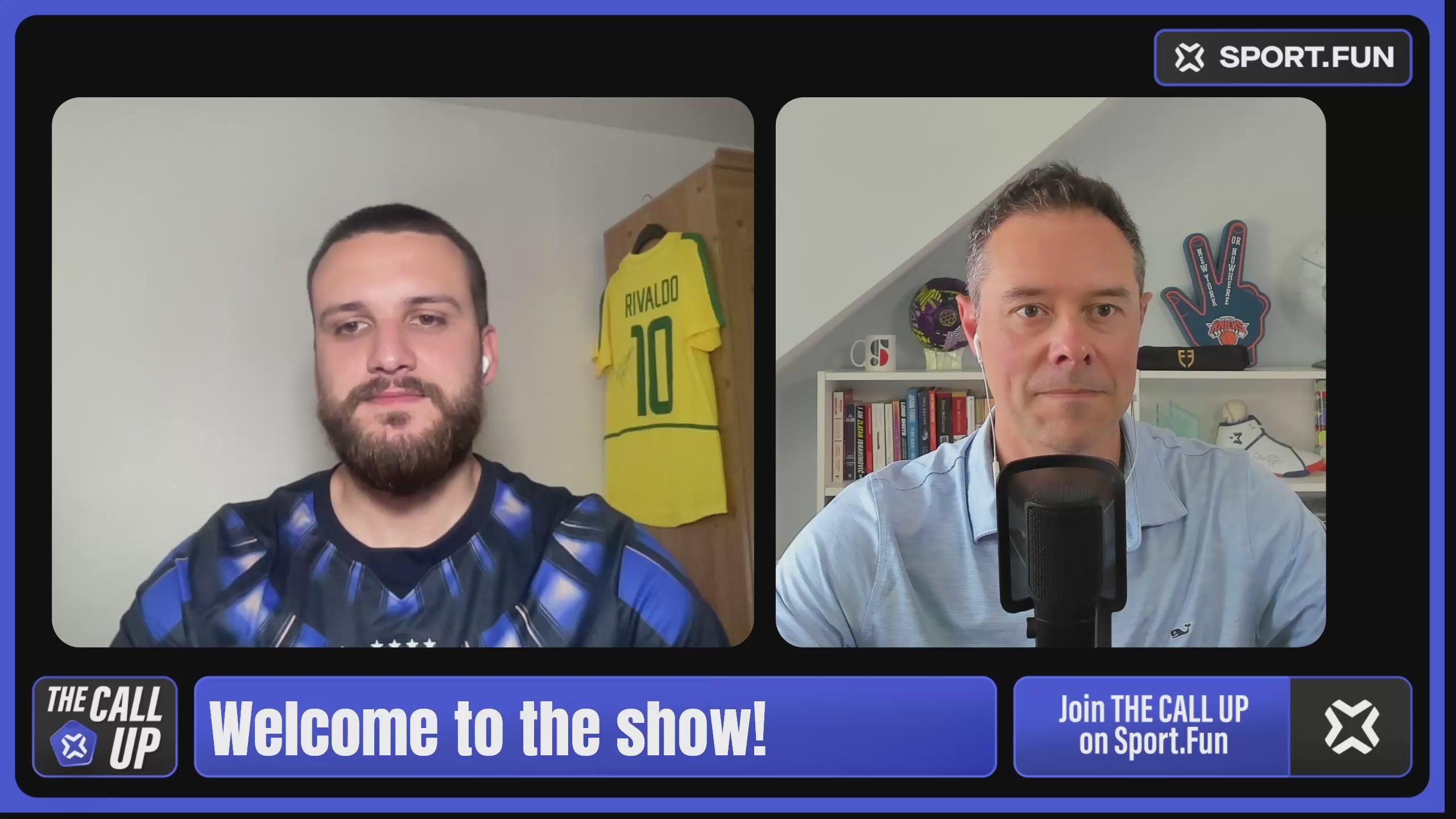 The image shows a man wearing a blue shirt with a yellow soccer jersey hanging on his wall next to another man who appears to be wearing a white shirt. They are both sitting at microphones, suggesting they might be hosting or participating in an interview or discussion related to sports. The background of the image is blurred and does not provide any additional context about their surroundings.