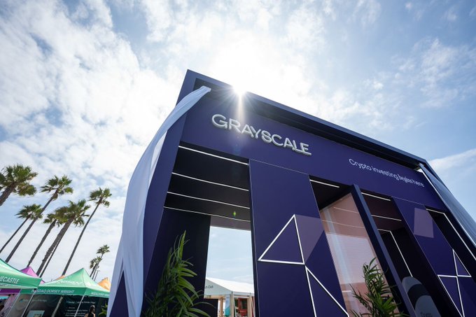A low-angle view of the 'GRAYSCALE' booth at an outdoor event with palm trees and a bright sky in the background.