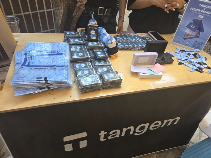 A Tangem crypto hardware wallet promotional booth displaying stacks of blue card wallets, branded merchandise, and signage at what appears to be a convention or event.