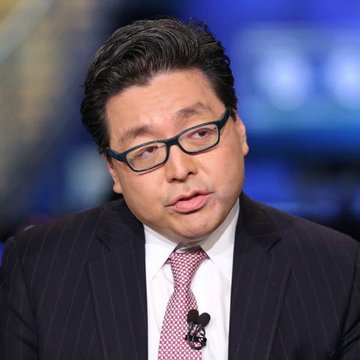 The image features a man wearing glasses, a suit, and a tie with a mouse charm on his lapel. The man appears to be talking or giving a speech, possibly at an event or on television. In the background, there are two clocks visible, one near the top left corner of the image and another towards the bottom right corner. The post about Tom Lee's Bitmine is related to this image as it discusses the unrealized loss on the Ethereum position of the cryptocurrency token.