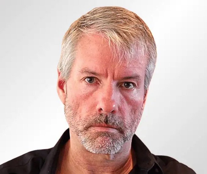 A close-up portrait photograph of a middle-aged man with short blonde/gray hair, stubble beard, and a black shirt against a plain white background.