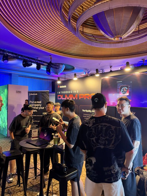 A group of people wearing dark shirts gather at a tech event booth with signage reading 'Introducing DLM PRO' and 'Your buddy. AI', set under a striking circular ceiling with blue lighting.