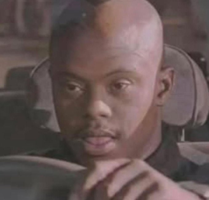 A close-up shot shows a bald man in a dark setting with a serious expression.