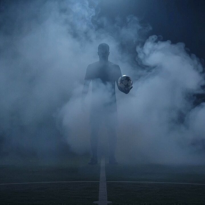 The image features a man standing on a soccer field, holding a soccer ball above his head while surrounded by smoke. The smoke creates an atmospheric effect that adds depth and mystery to the scene. The photo appears to be related to a World Cup event or promotion, as indicated by the accompanying text in the image description.