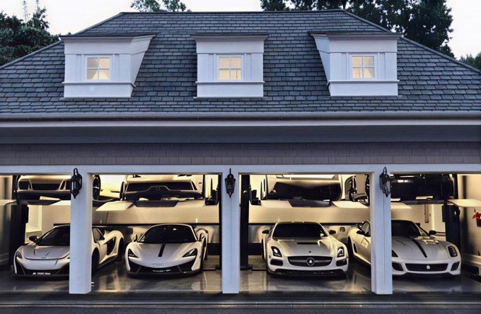 A luxury garage housing a collection of high-end sports cars, including multiple McLarens and Ferraris, parked on two levels in front of a residential home.