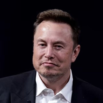 A close-up portrait of Elon Musk wearing a dark suit jacket and white shirt, set against a black background. The image relates to the post about X-Money's cryptocurrency remittance feature, as Musk is the owner of X (formerly Twitter) and a known supporter of DOGE.