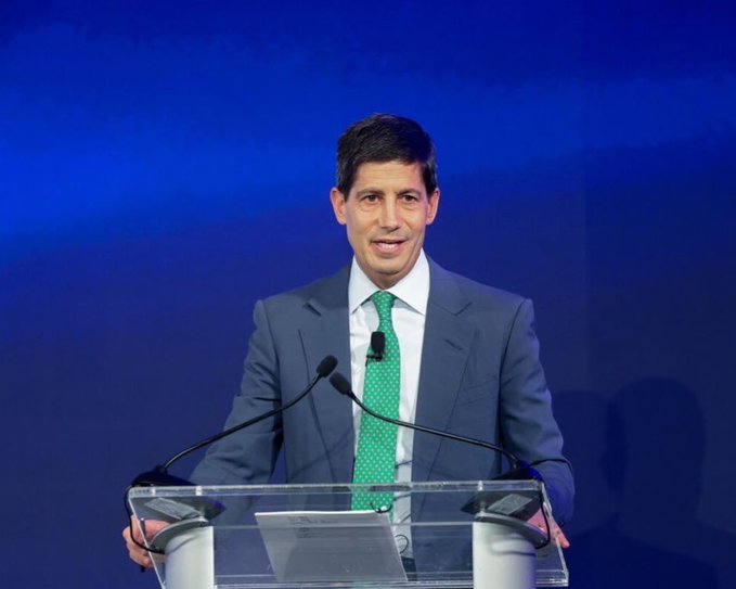 The image shows a man standing behind a podium, wearing a suit and tie, giving a speech or presentation at an event. The setting appears to be indoors with a blue wall as the backdrop for the scene. There are two microphones on either side of the man, indicating that he is addressing a large audience. The post includes text about a breaking news story related to the Federal Reserve Chair's first press conference in months and suggests that the event may be taking place at the Fed Chair's office.
