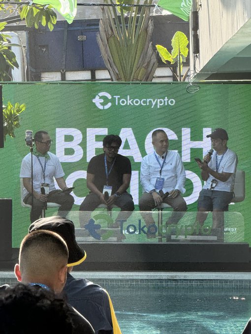 Panel discussion at a Tokocrypto "BEACH" event with four men seated on stage, one speaking into a microphone, with audience members visible in the foreground.