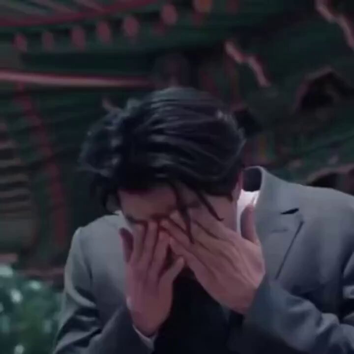 This image features a man dressed in business attire with black hair standing in front of a building or temple. He is looking down at his hands, which are resting on top of his face as if he has just experienced an emotional moment. The image also contains text that says "Bitcoin broke $70,000", possibly indicating the success of a particular event related to Bitcoin. However, it does not seem directly connected to the main focus of the image, which is the man in business attire and his facial expression.