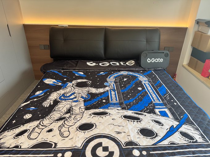 A king-size bed is completely covered by a large, space-themed picnic mat featuring an astronaut, a lunar base, and the "Gate" and "GATE.IO" logos, with an inflatable "Gate" sofa sitting on the edge. The setup illustrates the caption's note that the oversized picnic mat is big enough to cover a 1.8m king bed, alongside the new inflatable sofa ready to be blown up.