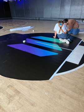 Two people work together applying large blue and purple geometric decals to a circular wooden floor.
