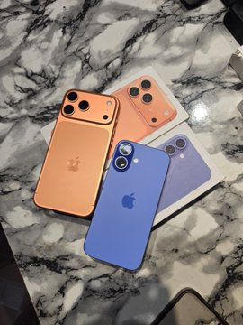 Four iPhone 17 Pro dummy units in orange, coral, blue, and purple displayed on a marble surface, showcasing the redesigned rear camera layout and MagSafe rings.