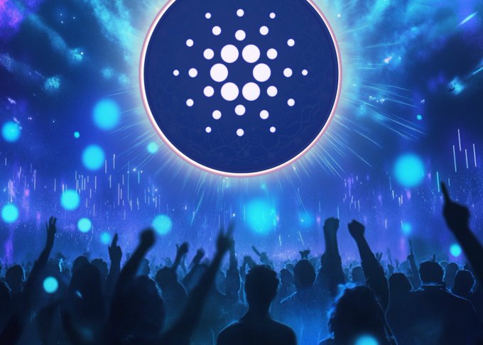 The image shows a large group of people gathered together with their arms raised, possibly at an event or concert. The crowd appears to be enjoying themselves as they celebrate the Cardano community's success. The atmosphere seems lively and energetic, with everyone seemingly engaged in the moment.
