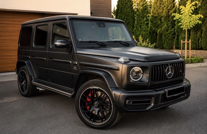 A 2022 Mercedes-AMG G63 finished in matte black ("murdered out") is parked in front of a modern home, featuring blacked-out wheels with red brake calipers and an aggressive AMG grille, matching the listing details for a $184k USD sale in Europe.