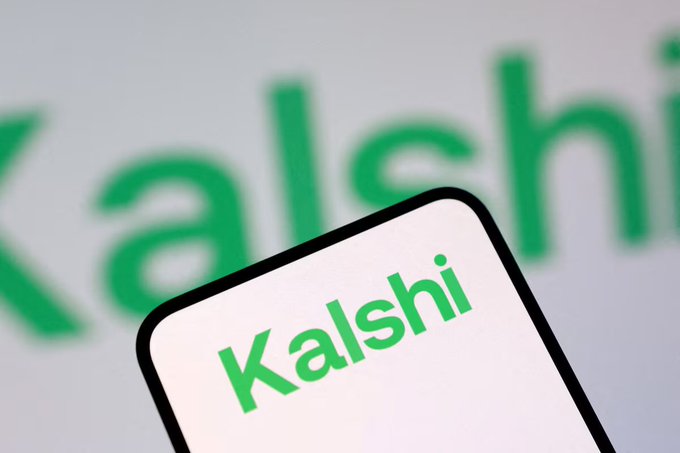 A smartphone displaying the green "Kalshi" logo is shown in front of a blurred background featuring the same branding. The image relates to the post by visually representing Kalshi, the prediction market platform seeking regulatory approval to launch stock and ETF-linked perpetual contracts.