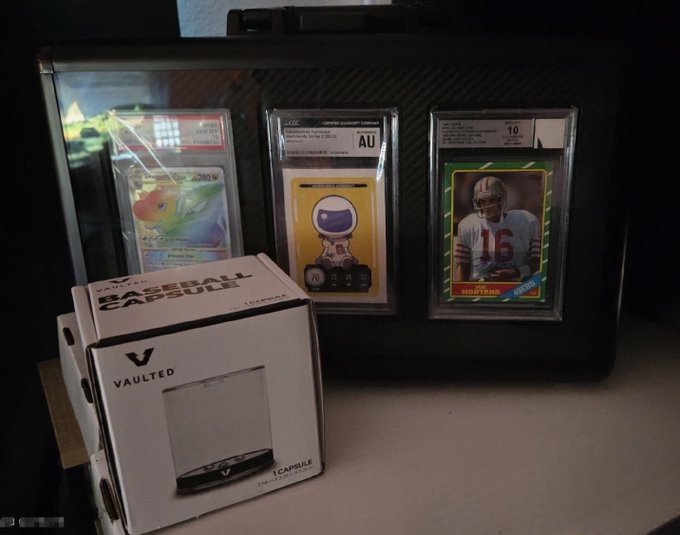 A collection of graded sports and Pokémon cards displayed in a case alongside a Vaulted baseball card storage box.