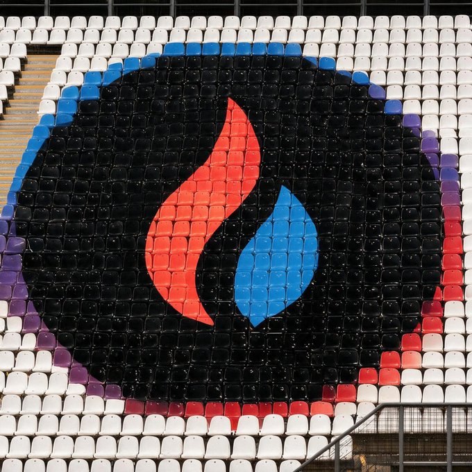Stadium seating arranged in the colors of the Turkish flag (red and white) forming a large circular logo with a flame and drop design in the center.