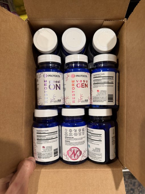 The image shows a cardboard box filled with dark blue supplement bottles labeled "Protocol" with "Restore VasculGEN" prominently visible, suggesting a bulk order of a vascular health supplement. This ties into the caption "Heavy experiments are beginning" implying the user is stocking up to begin an intensive protocol regimen.