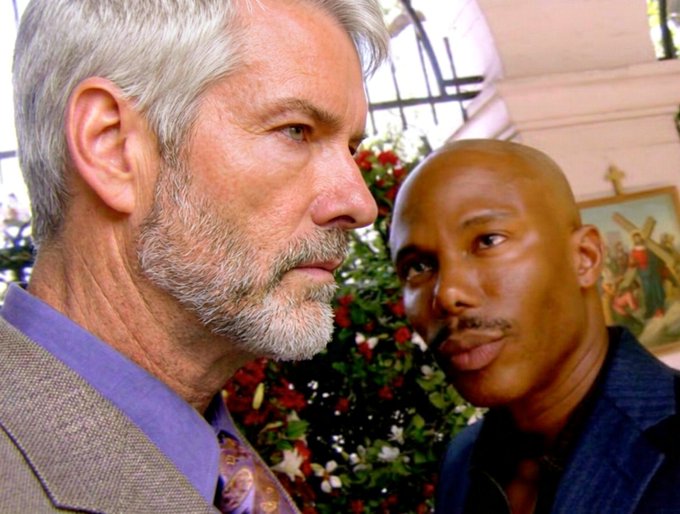 Two men with serious expressions stand together in front of a church window and floral arrangements, with the older gray-haired man in a suit gazing off to the side while the younger man looks on with a knowing smirk. The image humorously pairs with the caption "Never sell your Bitcoin," evoking a moment of firm conviction or silent wisdom about holding onto one's cryptocurrency investment.