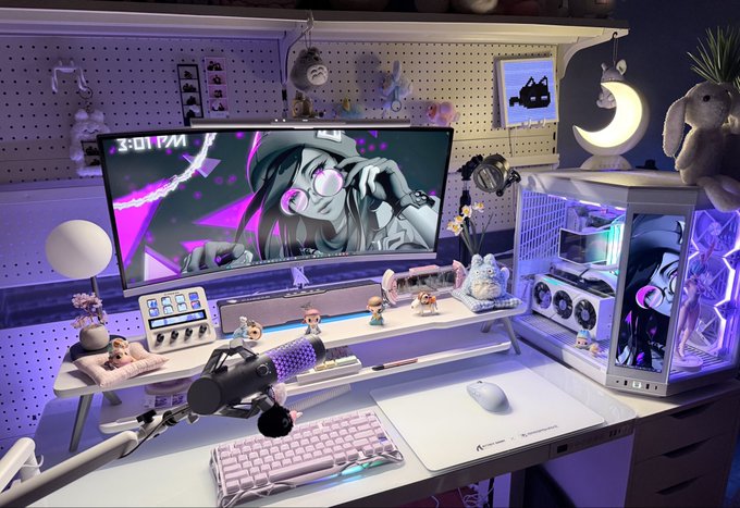 An aesthetic gaming setup features a curved monitor displaying anime artwork with the time '3:01 PM', a white PC case with RGB lighting, a pink keyboard, a microphone, and various anime figurines and plushies on a pegboard wall.