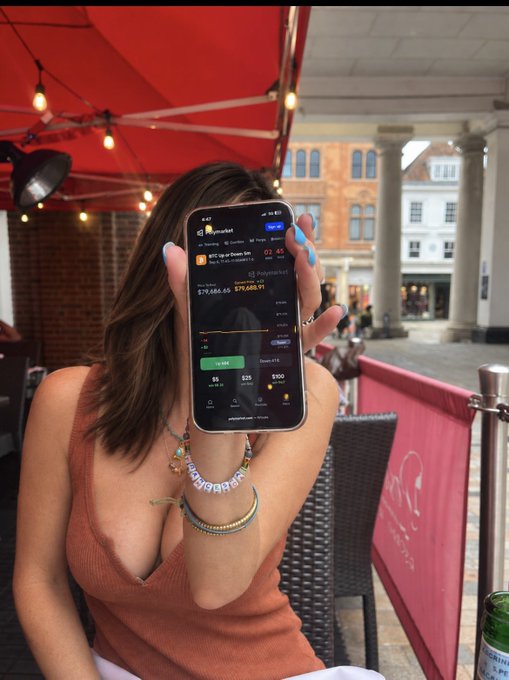A woman in an orange top holds up a phone at an outdoor café, displaying a Robinhood crypto screen showing Bitcoin (BTC) at $78,686.68, down $1,344 (-1.68%), tying into her post about gambling on whether BTC will go up or down.