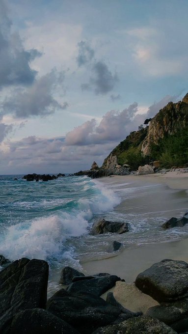 A scenic coastal view of waves crashing against rocky shoreline at twilight with a dramatic cloudy sky.