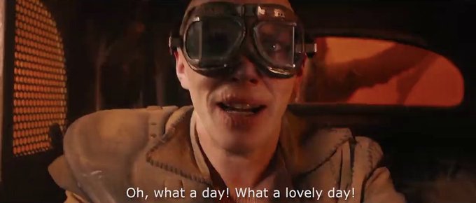 A person wearing vintage aviator goggles grins excitedly inside a vehicle with warm, amber-lit surroundings. The subtitle reads: "Oh, what a day! What a lovely day!"