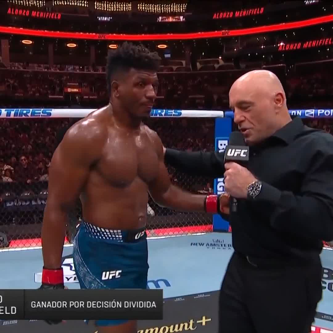 UFC fighter Alonzo Menifield, shirtless in blue shorts, is interviewed in the octagon by Joe Rogan following his split decision victory ("GANADOR POR DECISIÓN DIVIDIDA" displayed on screen), with "ALONZO MENIFIELD" banners visible in the arena background. The image corresponds to the post's caption about Menifield securing the win, highlighting the broadcast setting for #UFC331.