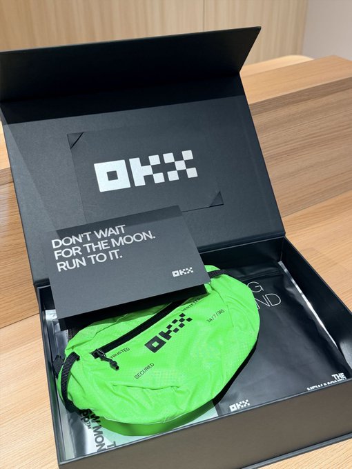An opened black shoe box with the text 'DON'T WAIT FOR THE MOON. RUN TO IT.' reveals a neon green bag inside with 'OKXX' branding.