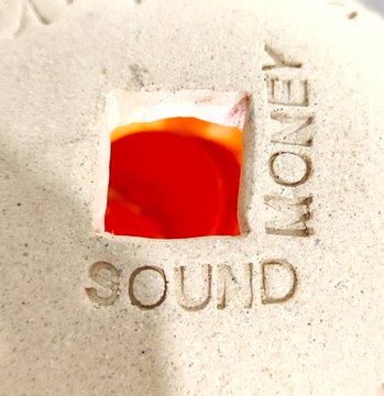 The image features a small ceramic object with the words "Sound" carved into its surface. The object appears to be made of clay or porcelain, giving it an artistic appearance. The text "If you're in @BTCPrague, come see it in the art gallery. FEEL what a trustless ledger FeELS like. HOLD  5000 years of wisdom. SEEN through merkle trees and lets you see the transaction." is written around the object, which seems to be related to the post about sound or music. The image does not contain any other objects or people, so it focuses on the ceramic item with the accompanying text.