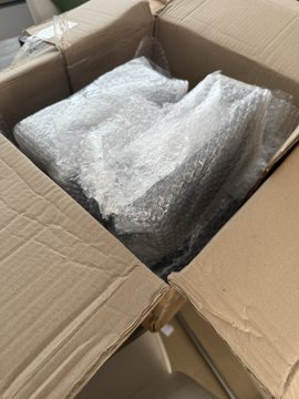The image shows a cardboard box with a white item inside, which appears to be bubble wrap or packing paper. The box has been opened, revealing its contents. The text "Just received a lil’ something in the mail today" suggests that someone recently received an item from another location and is now opening it to see what's inside. The image also mentions that the event will take place on Monday & Tuesday at the Litecoin Summit in Amsterdam, which could be related to the bubble wrap or packing paper if it was a gift or package sent by someone attending the summit.